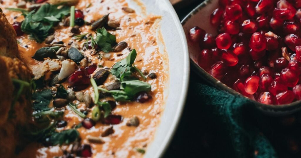 white bowl filled with babaganoush and garnished with pomegranate and parsley on left. Smaller bowl of pomegranate on right.