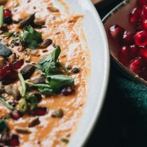white bowl filled with babaganoush and garnished with pomegranate and parsley on left. Smaller bowl of pomegranate on right.