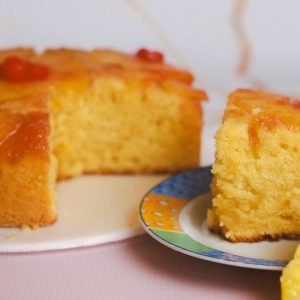 Upside-Down Cake topped with maraschino cherries with a slice on a plate.